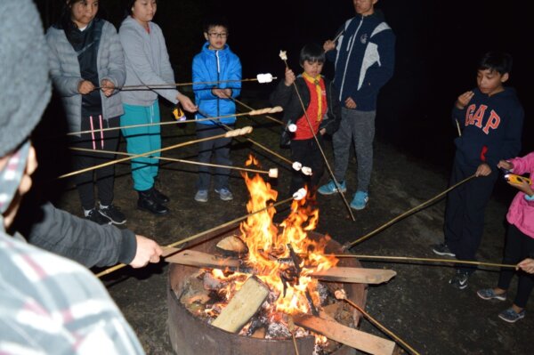 Pathfinders roasting marshmallows over a fire at night outside