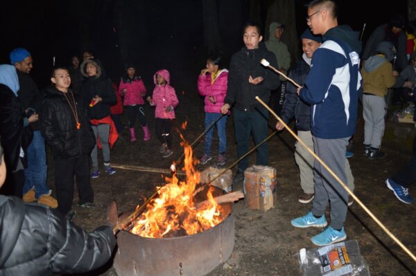 Pathfinders roasting marshmallows over a fire at night outside