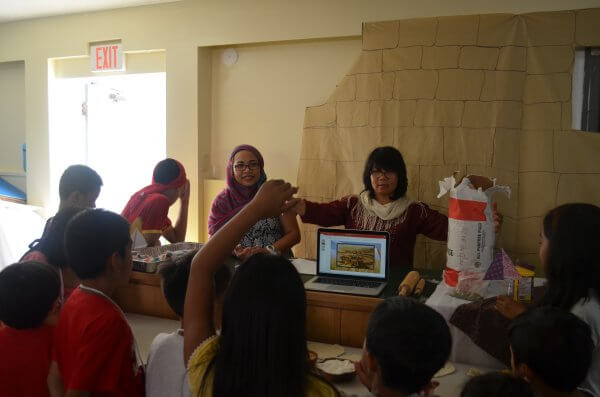 Two women giving a Bible lesson and presentation on making bread to children